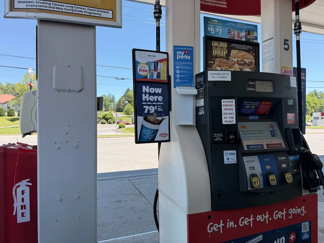 Phone displaying credit card cash back breakdown next to a gas pump digital display.